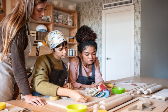 Women shaping clay and glazing ceramic pieces in studio