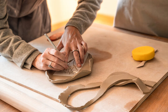 Potter carving pattern into clay slab in pottery workshop