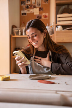 Young potter checking phone in pottery workshop studio