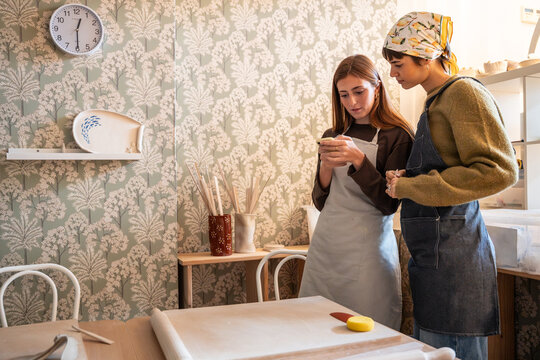 Young women in pottery workshop checking phone together