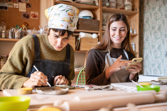 Pottery workshop artist painting clay while colleague texts