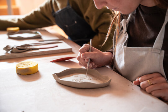 Pottery artist carving pattern on clay tray in workshop