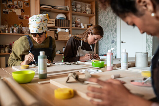 Pottery workshop students painting ceramic pieces at table