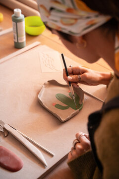 Potter hand painting clay slab in pottery workshop