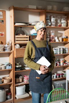Potter in apron holding tablet computer in ceramics studio