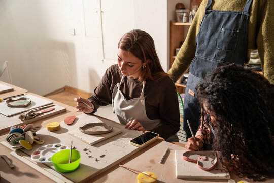 Pottery workshop students shaping clay and carving relief tile