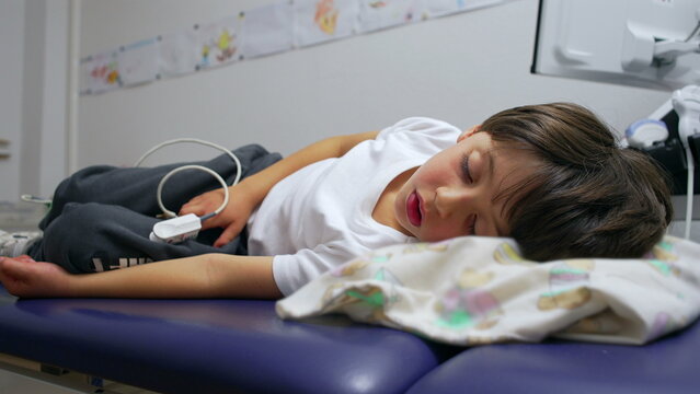 Young boy resting on hospital bed connected to monitor, child recovering after medical treatment, vulnerable and tender moment in healthcare environment