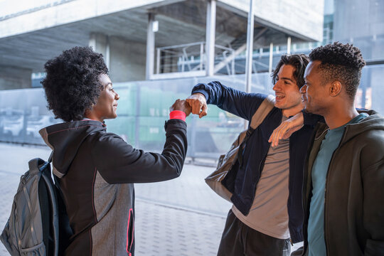 Friends greeting with elbow bump outside a modern campus
