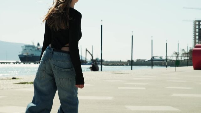 Gimbal tracking shot of woman roller skating on seafront &mdash; opens on windy side portrait with earbuds and sunglasses, camera pans down to inline skates gliding. Marina and mountain behind. 