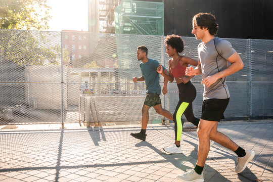 Three friends jogging outdoors in city during sunny morning