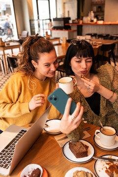 Two women taking selfie with coffee and dessert in cafe