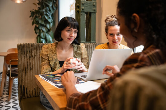 Multiethnic women meeting in cafe planning work on laptop