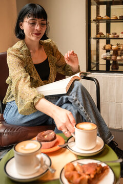 Young woman reading book in cozy cafe with coffee and pastry
