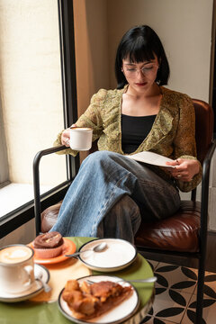 Woman reading book with coffee at cafe window seat