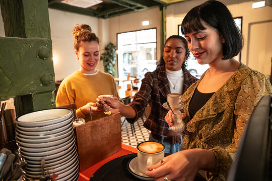 Multiethnic friends serving coffee together in a cafe