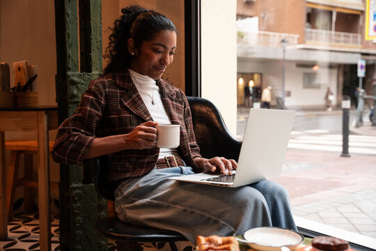 Young woman using laptop and coffee in city cafe window