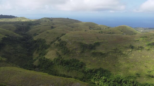 Cinematic aerial drone orbiting left while panning right over the rolling hills of Teletubbies Hill on Nusa Penida, Indonesia.