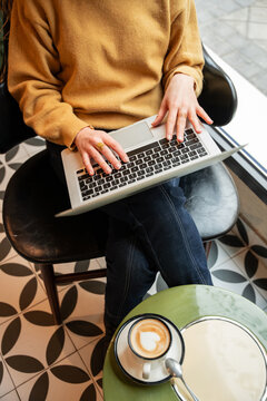 Person typing on laptop in cafe with coffee on table