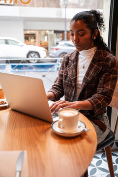 Young woman working on laptop at cafe window with coffee