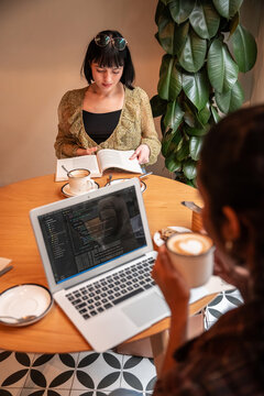 Multiethnic colleague working in cafe with laptop and book