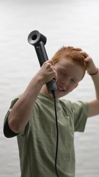 A red-haired teenager sings and dances in the bathroom while aiming a hot hair dryer at her hair. High quality FullHD footage