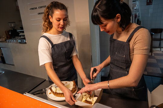 Two barista preparing cake slices in cozy coffee shop