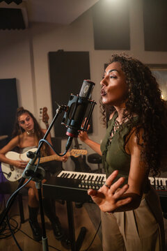 Female singer recording vocal in studio with guitarist