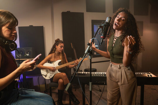 Vocalist singing in recording studio with guitarist nearby