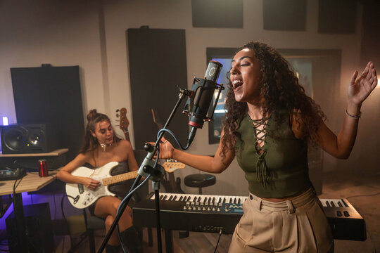 Singer recording vocal in music studio with guitarist