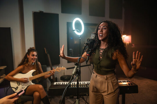 Female singer recording vocals with guitarist in studio