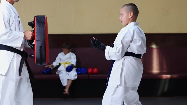 An athlete with black pads on his hands throws straight punches at a training apparatus held by a trainer