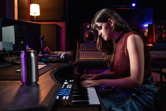 Young woman playing keyboard in recording studio at night