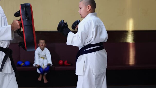 An athlete with black pads on his hands throws straight and roundhouse punches on a training apparatus held by a trainer