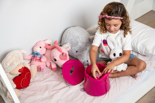 Child playing with toy bucket on bed with stuffed animal