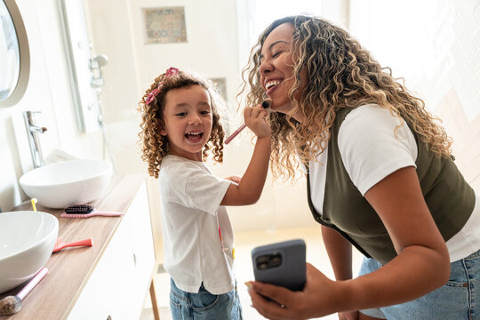 Mother and daughter laughing during makeup play in bathroom