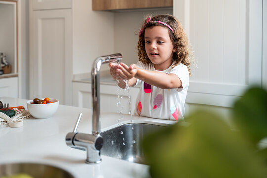 Child washing hands at kitchen sink in bright modern home
