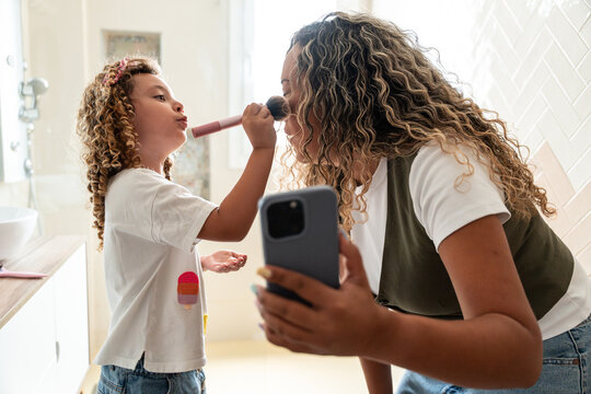 Playful child apply makeup to mother during selfie