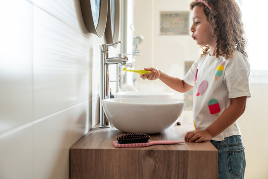 Young child brushing teeth at bathroom sink in morning light