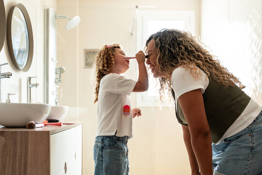 Playful child applying makeup to mother in bright bathroom