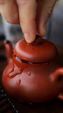 Close up of a person performing a traditional chinese tea ceremony, putting the lid on a yixing clay teapot after brewing hot pu erh tea and pouring hot water over it