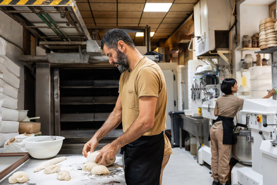 Baker shaping dough in artisan bakery kitchen workspace