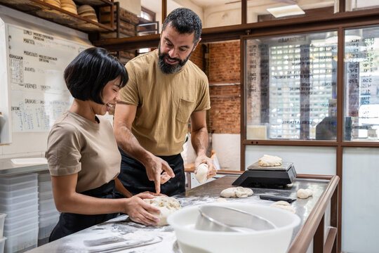 Baker teaching apprentice shaping dough in artisan bakery