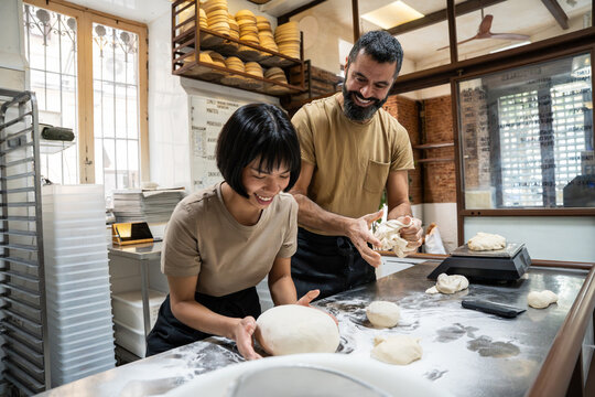 Baker coaching apprentice shaping dough in artisan bakery