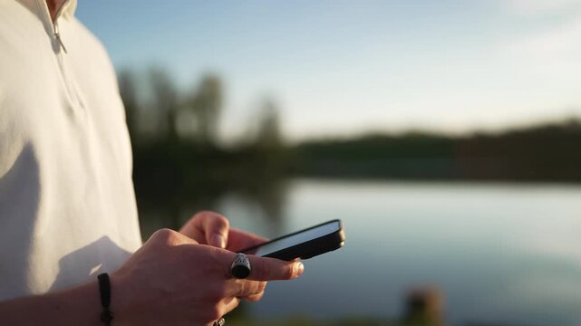 Man Using Smartphone Near Calm Lake at Sunset - Digital Nomad and Technology in Nature Concept