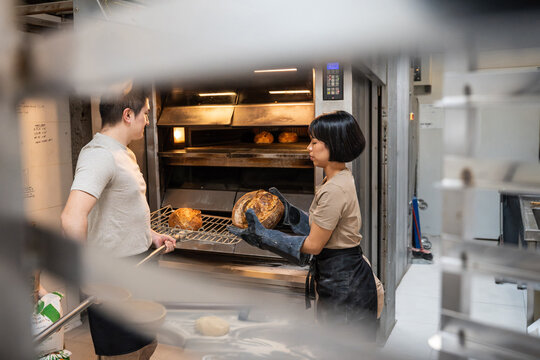Baker taking artisan bread from oven in bakery kitchen