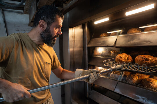 Artisan baker taking sourdough loaves from oven