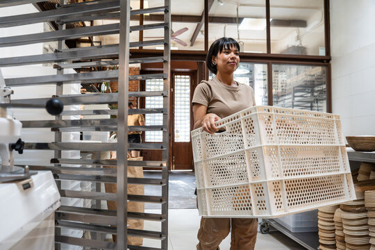 Baker carrying empty crate in artisan bakery workspace