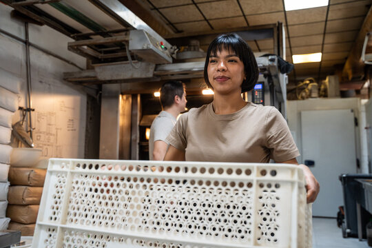 Woman carrying bread crate in artisan bakery workspace