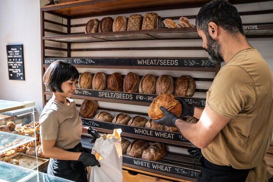 Baker hands artisan loaf to customer in small bakery shop