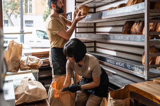 Artisan baker stocking fresh bread on bakery shelf